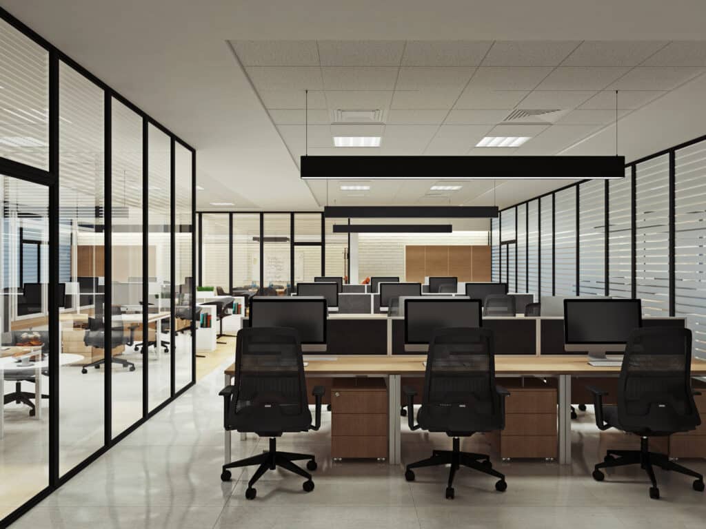 Bureau open space moderne: rangées de bureaux équipés, ordinateurs, chaises, cloisons vitrées avec stores. Ambiance lumineuse.