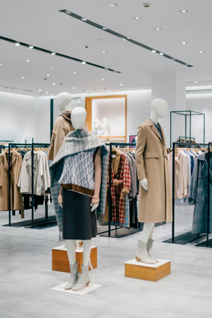 Trois mannequins présentent des manteaux et tenues d'hiver dans un magasin de vêtements moderne. Les cintres sont remplis.
